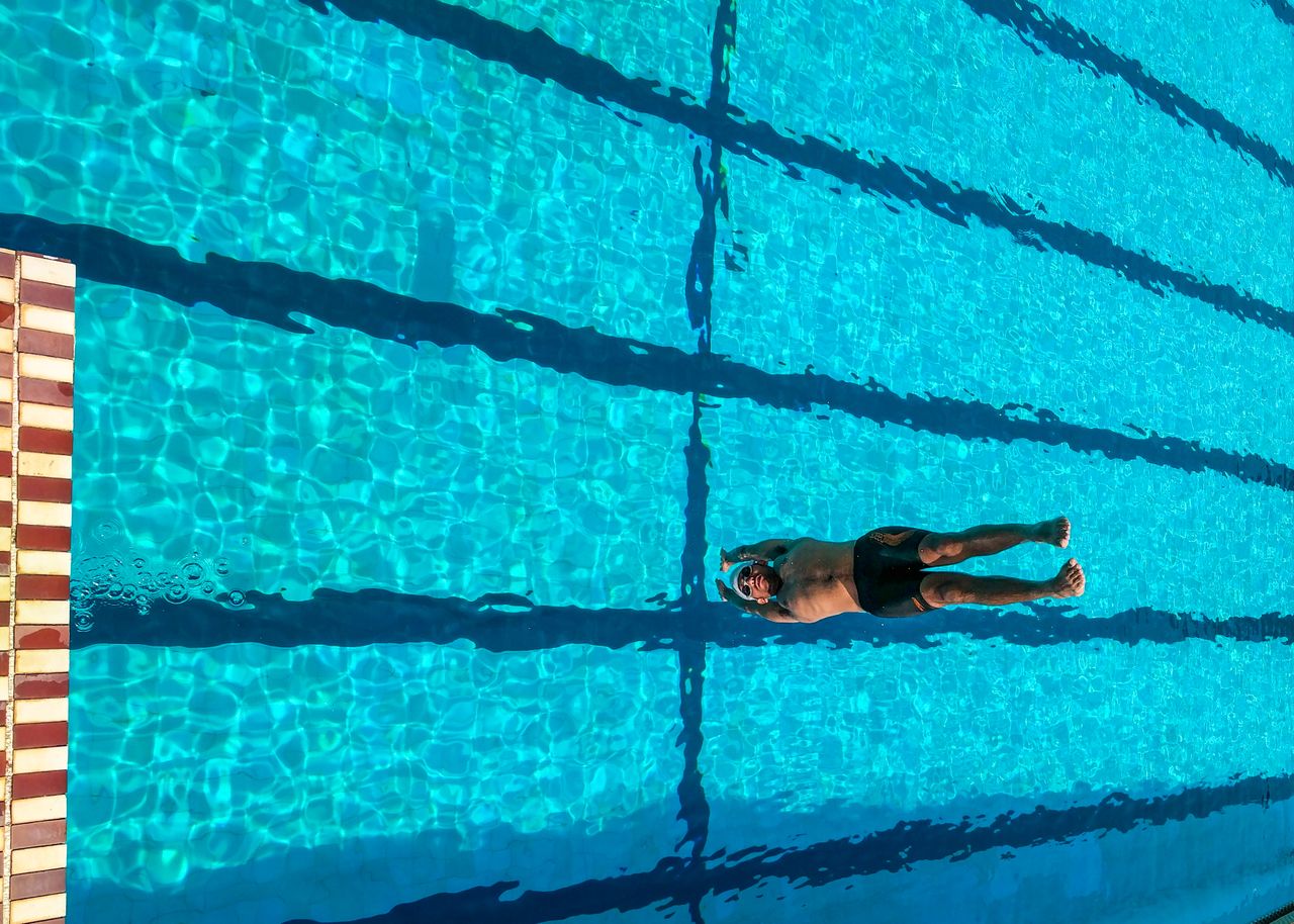 A man enjoys swimming on a sunny day in a vibrant blue pool.